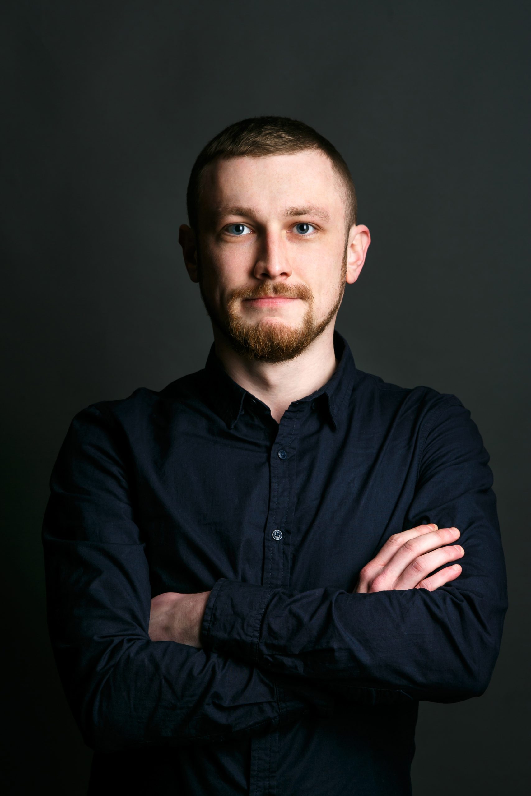 Dark blonde bearded man crosses his hands on chest posing in black shirt