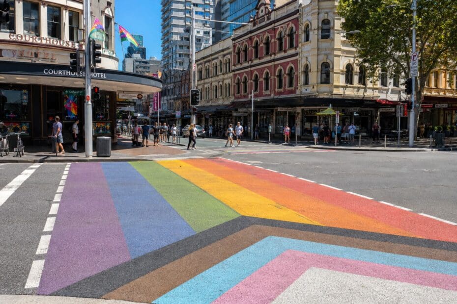 a vibrant daytime photograph of the Progress Pride crossing near Taylor Square, with Oxford Street’s heritage buildings in the background (Sydney)