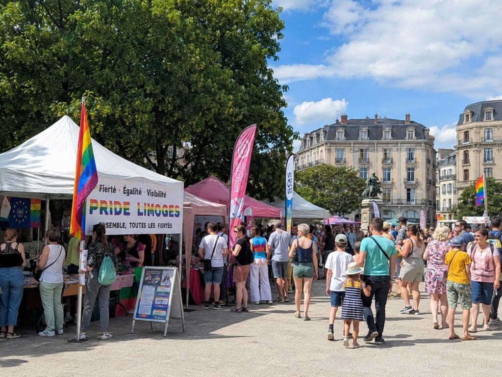 une photo SFW et familiale du village associatif de la Marche des fiertés sur la Place de la République (Limoge), avec drapeaux colorés et public de tous âges