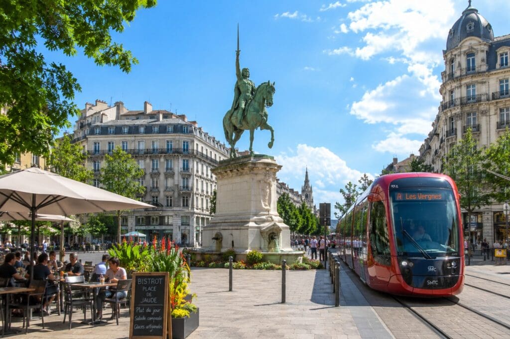 une photo de la place de Jaude avec le tramway, la statue de Vercingétorix et les terrasses