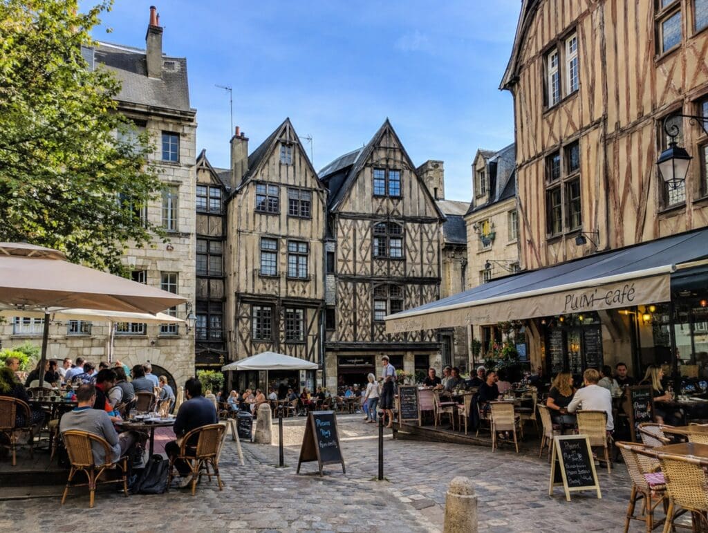 une photo ensoleillée de la place Plumereau à Tours avec ses terrasses animées devant les façades médiévales