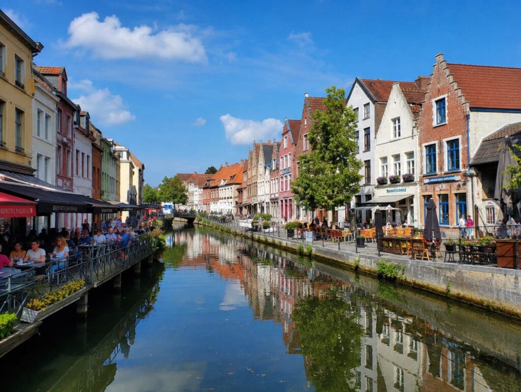 une photo ensoleillée des façades colorées de Saint-Leu à Amiens se reflétant dans les canaux, avec quelques terrasses au bord de l’eau